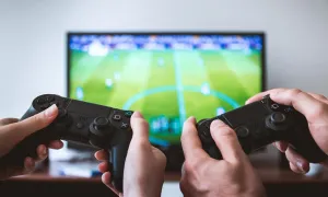 "two people playing a video game with controllers in the foreground and tv screen in background"