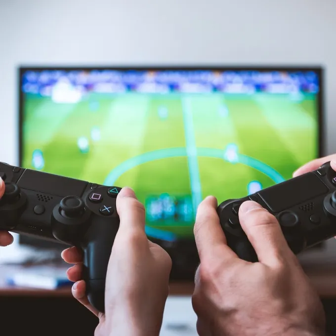 "two people playing a video game with controllers in the foreground and tv screen in background"